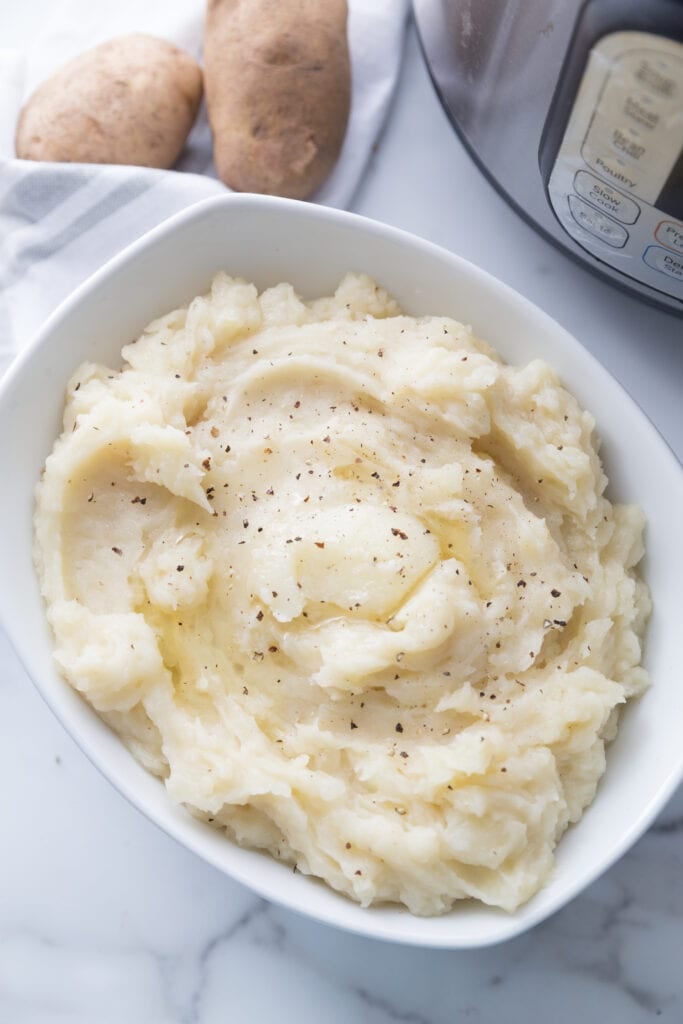 White rectangular oval serving bowl full of mashed potatoes topped with fresh black pepper and melted vegan butter making them dairy free