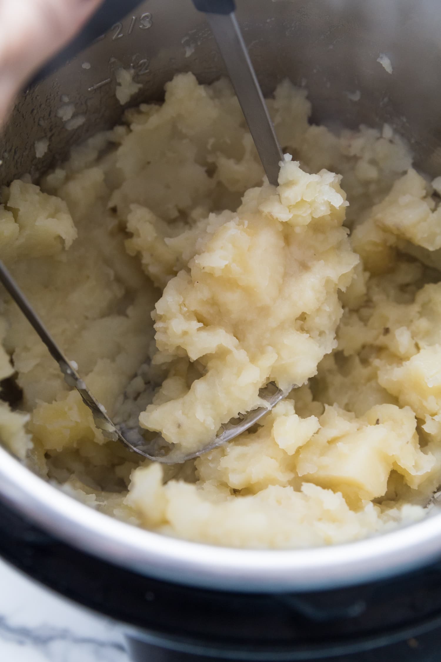 Close up photo of freshly mashed dairy free Mashed potatoes still in the Instant pot with a potato masher.