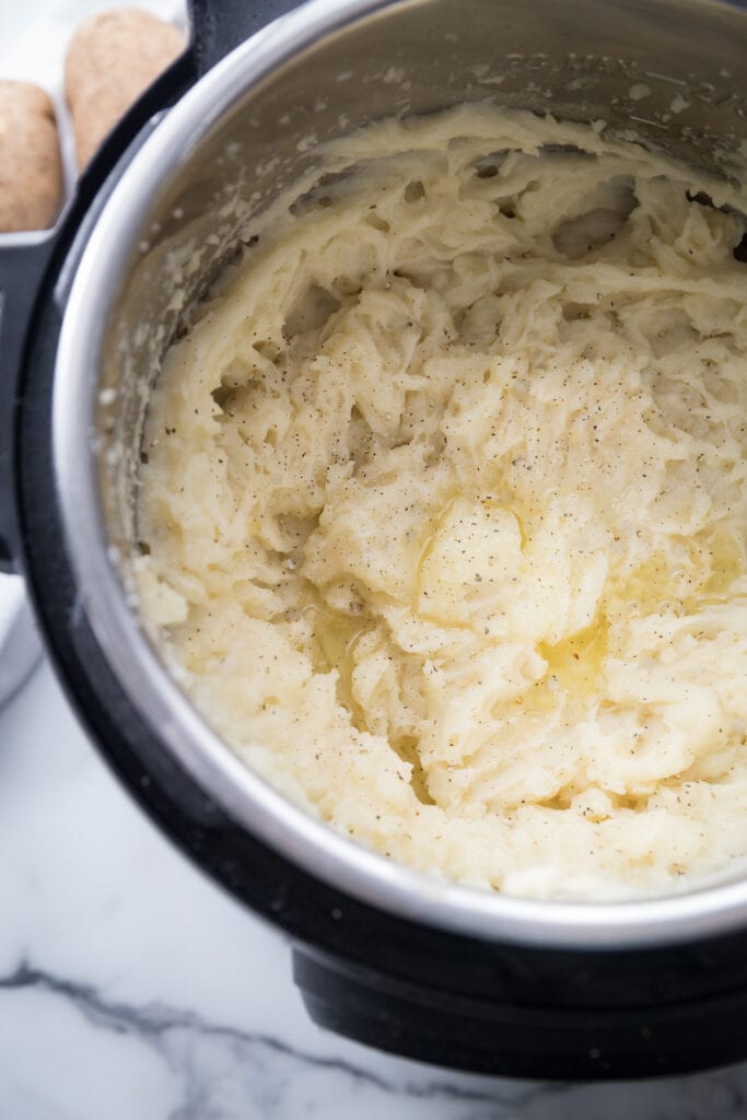 Overhead photo of freshly mashed Instant Pot Mashed potatoes still in the Instant pot, topped with ground black pepper and melted vegan butter.