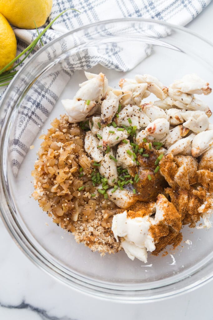 Jumbo lump crab meat in a bowl with sauteed onions, garlic, and chives, breadcrumbs and seasoning