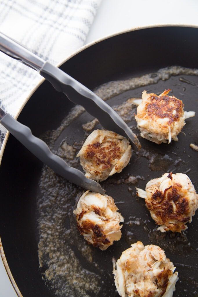 Mini gluten-free crab cakes being cooked in a pan 