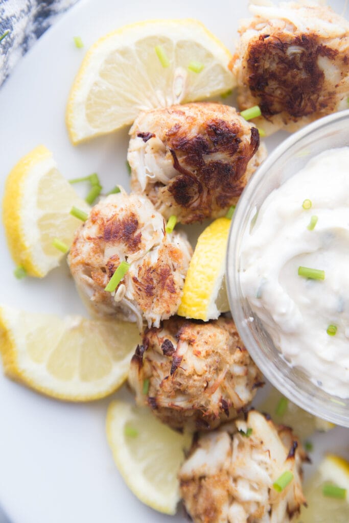 Overhead photo of mini crab cakes made in the air fryer garnished with sliced lemons and green onion with aioli in a bowl for dipping