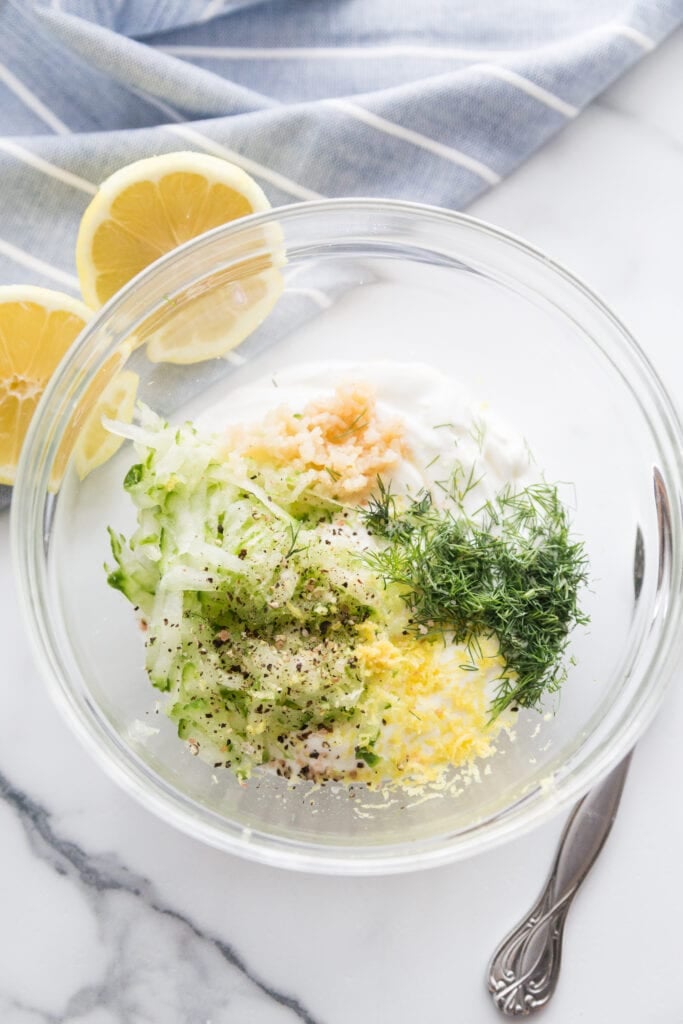 Overhead photo of glass bowl filled with ingredients to make homemade tzatziki dressing to top Easy Falafel Bites