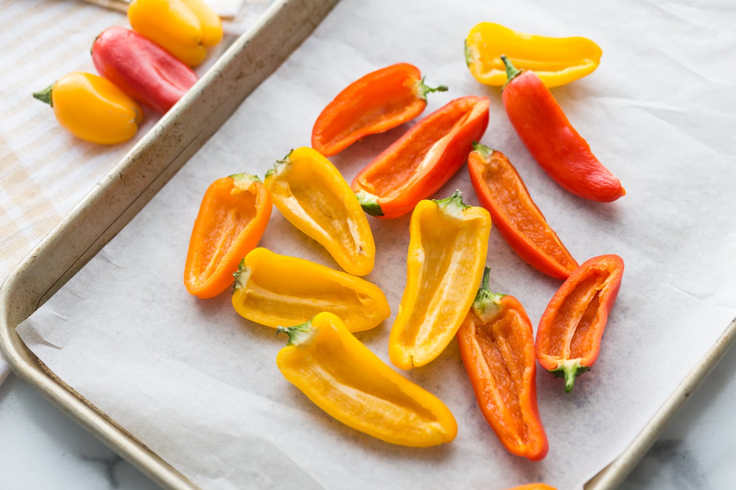 Red, Orange, and Yellow halved, seeded mini bell peppers on a parchment lined sheet pan