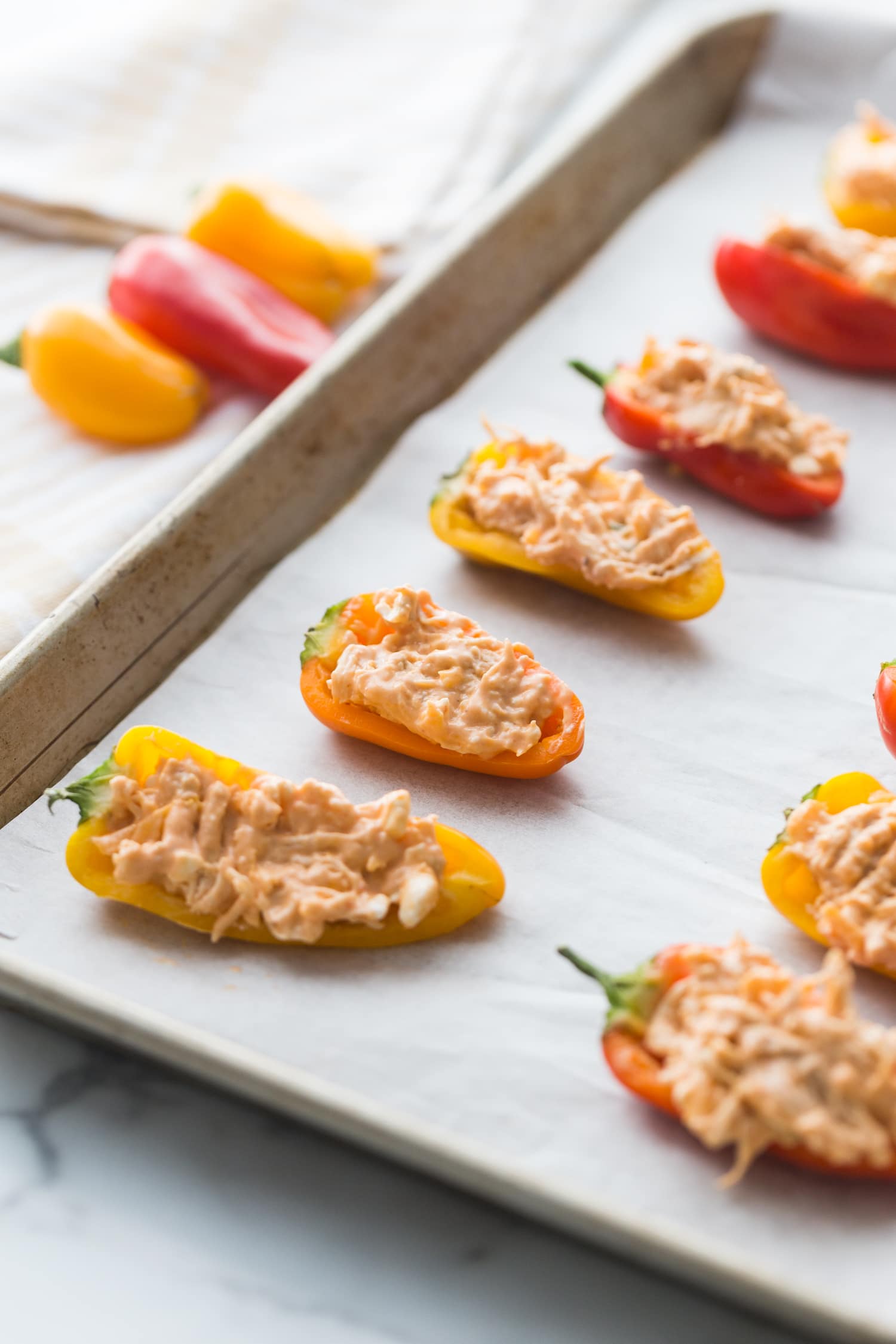 Close up side angle of a Sheet pan lined with parchment paper with rows of orange and yellow mini Healthy Buffalo Chicken Dip Stuffed Peppers