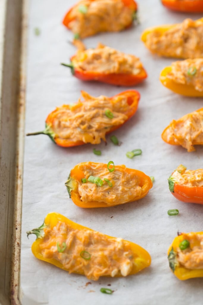 Close up of a Sheet pan lined with parchment paper with rows of orange and yellow mini Healthy Buffalo Chicken Dip Stuffed Peppers