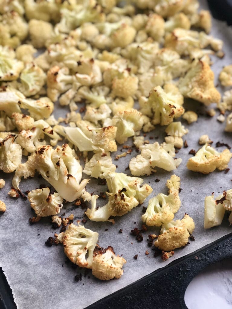 Roasted cauliflower on a parchment lined sheet pan ready for Buffalo Cauliflower Dip