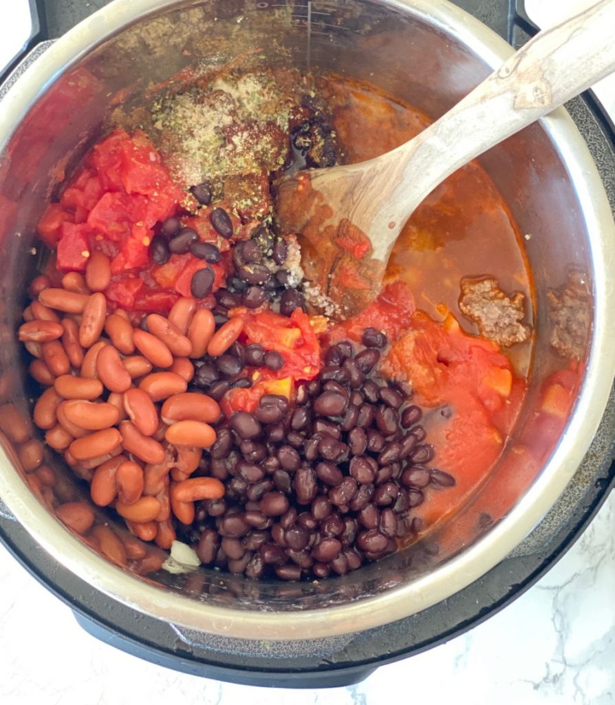 Overhead photo of instant pot with separated ingredients for 5 ingredient chili- black beans, kidney beans, diced tomatoes, tomato sauce, spices.