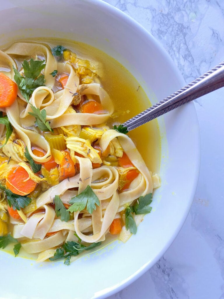 Close up photo of Instant Pot Chicken Noodle soup in a white bowl with a spoon on the side, on a white marble background. 