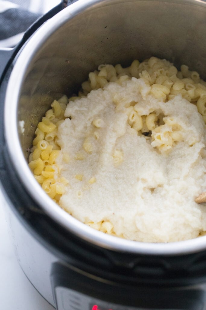Offset overhead view of an instant pot with cooked gluten free elbow noodles, topped with cauliflower puree, ready to be mixed.