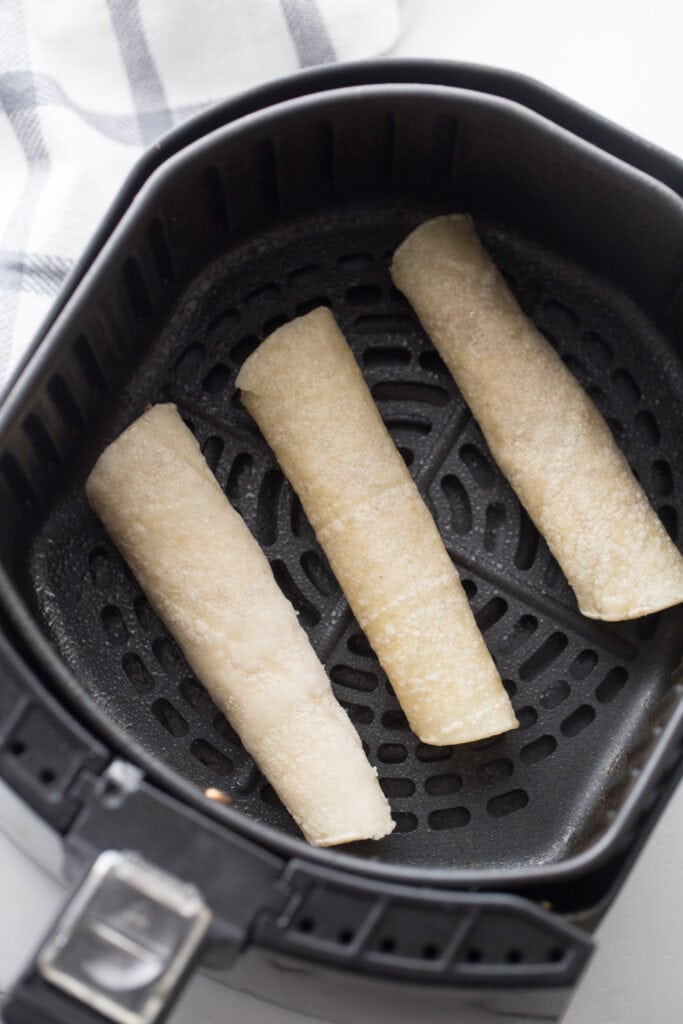 Three beef taquitos in an air fryer basket, ready to be cooked