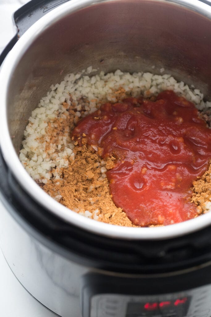 High angle photo of an instant pot filled with cooked beef, cauliflower rice, and tomato sauce, making the filling for beef taquitos.