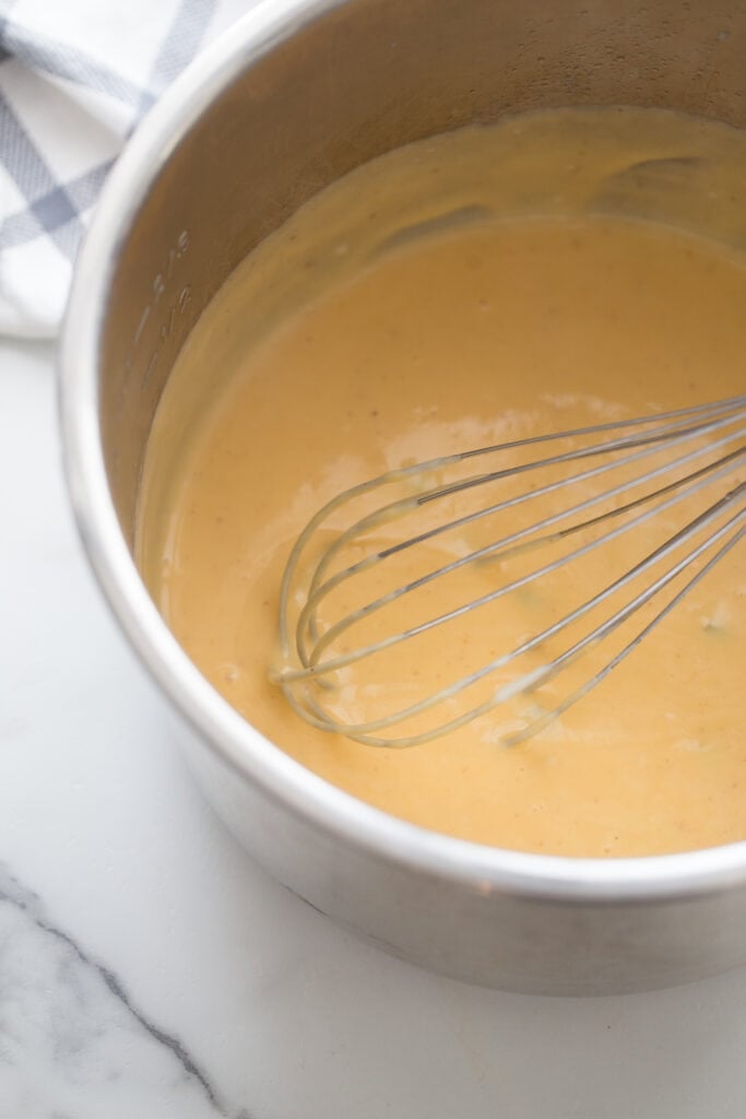 High angle photo of the inner liner of an instant pot with a whisk and finished homemade cheese sauce for beef taquitos.