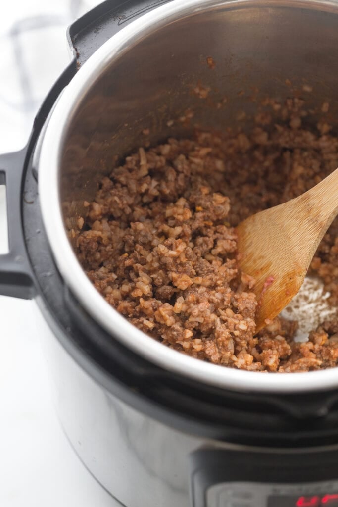 High angle photo of an instant pot and wooden spoon stirring beef taquito filling.