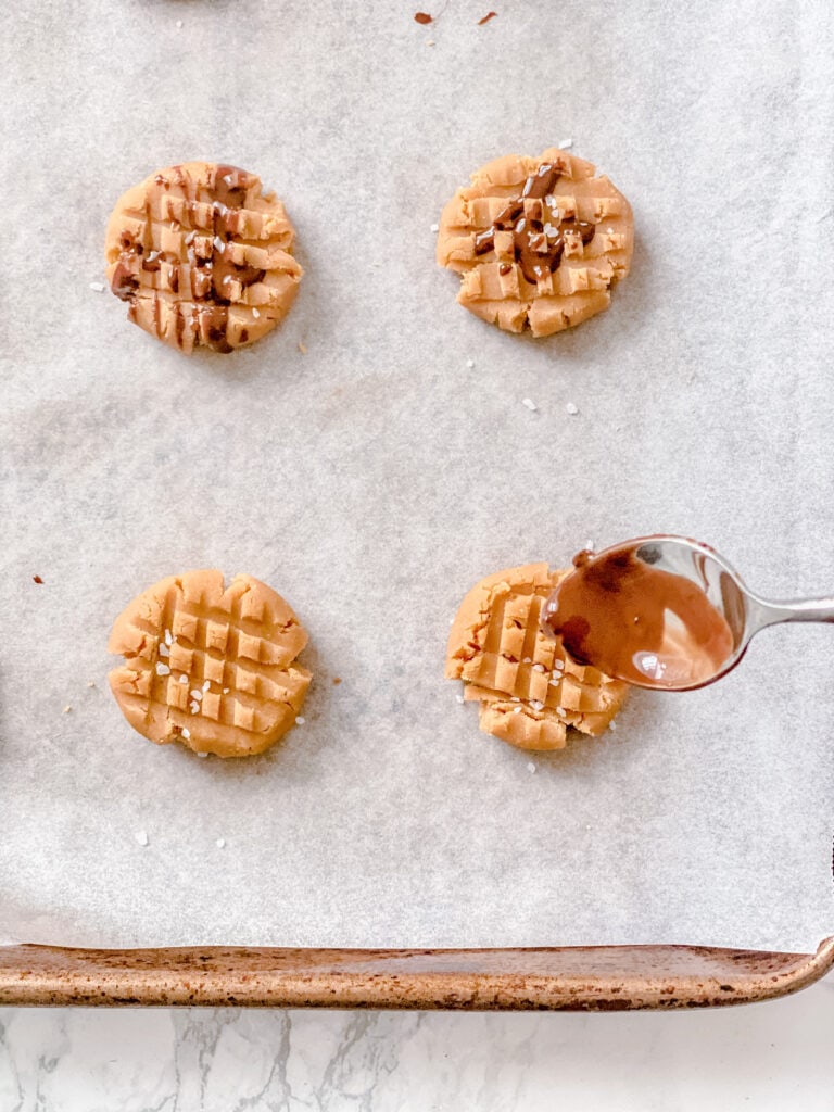 Close up overhead photo of Healthy Peanut Butter Cookies sprinkled with sea salt and in process of being drizzled with melted chocolate.