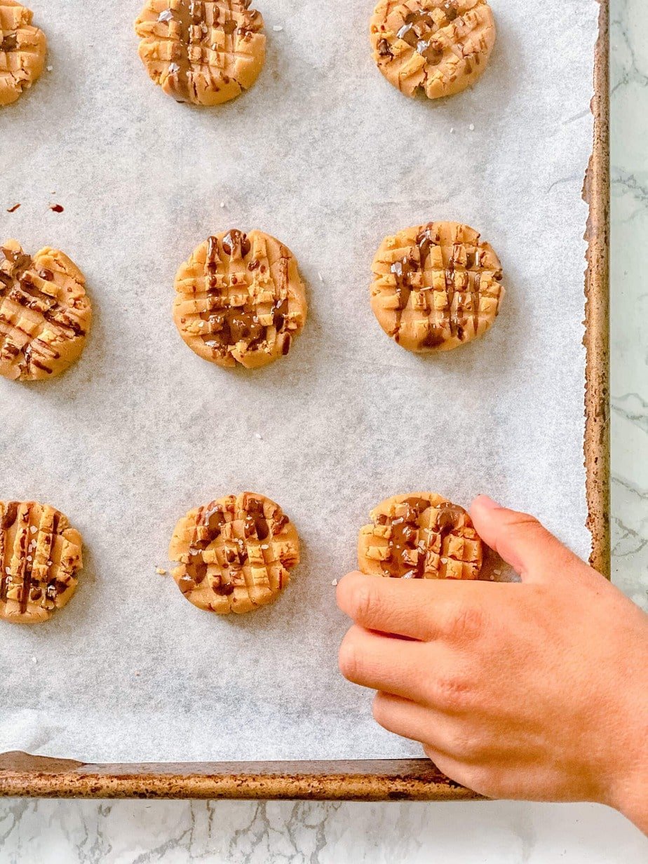 Rows of No Bake Peanut Butter Cookies on a parchment lined sheet pan with a boy's hand trying to sneak a cookie from the tray. 