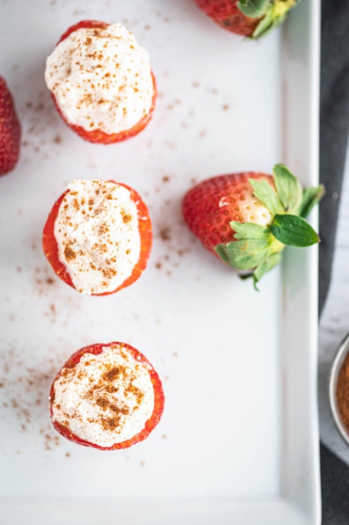 Overhead photo of cheesecake stuffed strawberries and whole strawberries on the side of a rectangular white serving dish.