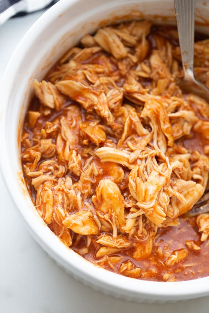 BBQ pulled chicken in a white round casserole dish with a spoon.