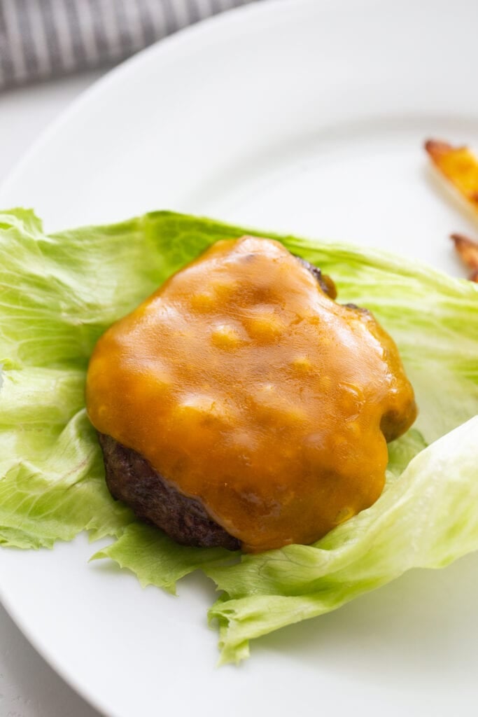Overhead photo of the best burger topped with cheddar cheese and resting on a large lettuce leaf. The lettuce will wrap the burger for a bunless option.