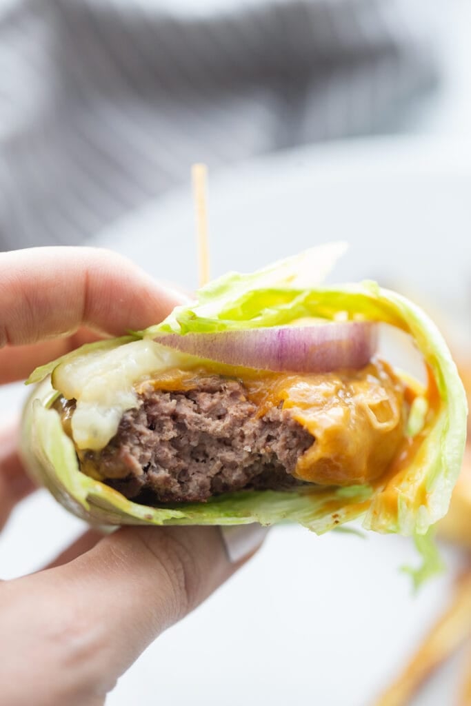Close up photo of a lettuce wrapped burger topped with cheddar cheese, burger sauce, red onion, and pickles, all held together with a toothpick sticking out of the center.