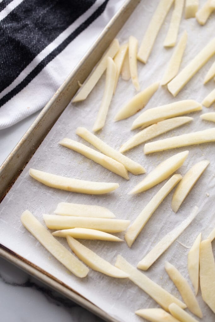 Overhead photo of a parchment lined sheet pan with fries, ready to make baked French fries.