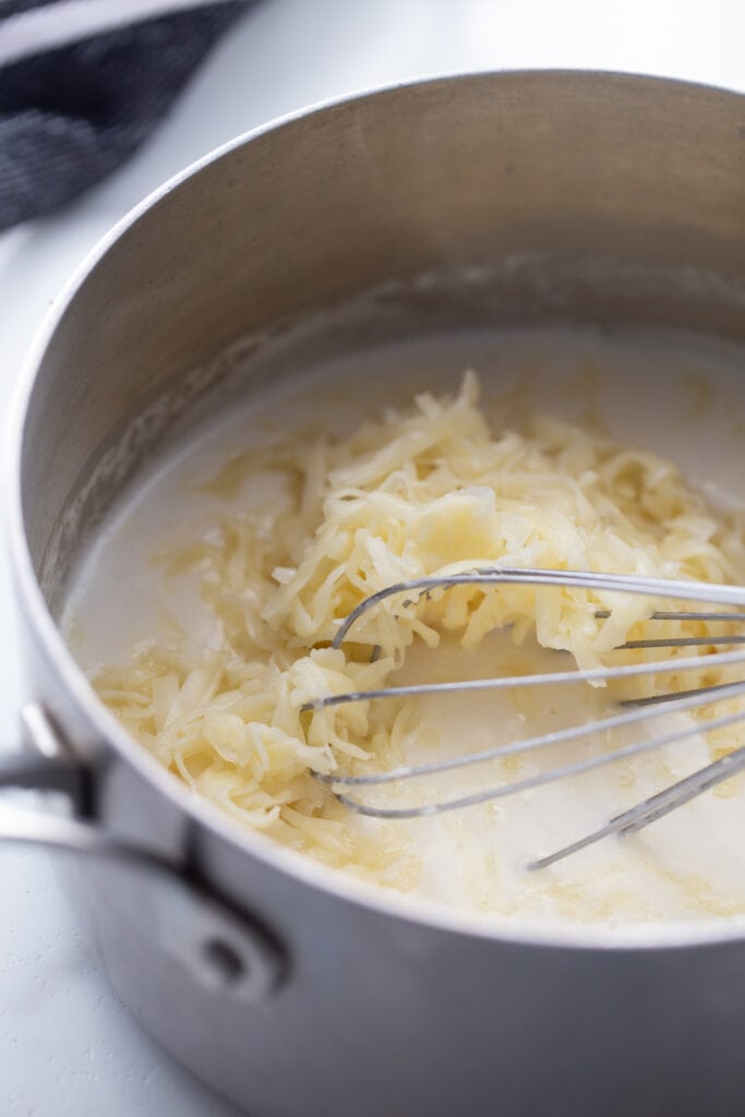 Close up photo of a saucepan and whisk with rue and melting cheese in the process of making homemade cheese sauce for a crab fry dipping sauce.