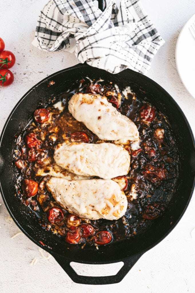 Overhead photo of caprese chicken in a cast iron skillet, ready to be served. The three chicken breasts are beautifully cooked and topped with melted cheese. The tomato and balsamic has reduced to a nice texture.