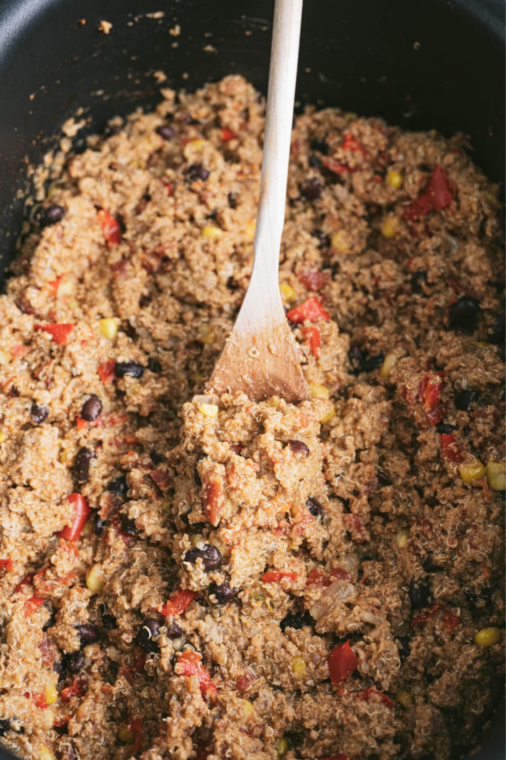 Mexican quinoa casserole in a black crock pot with a wooden spoon.
