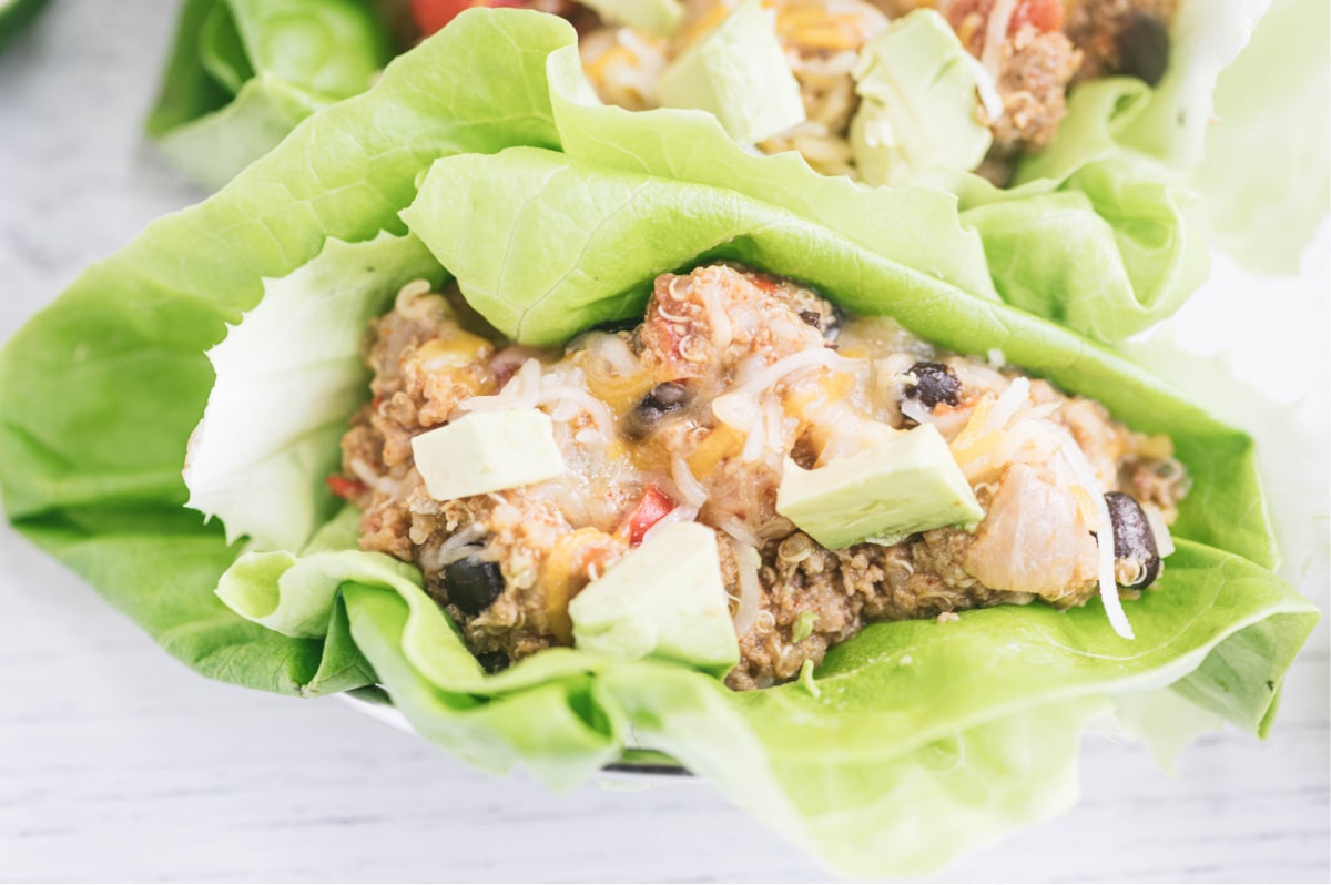Close up photo of crock pot taco casserole in a lettuce wrap and topped with avocado.