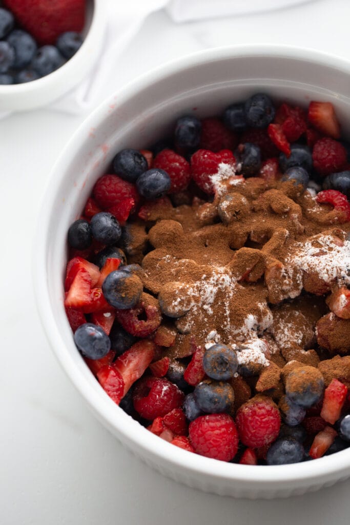 Close up photo of a large white casserole dish filled with blueberries, strawberries, and raspberries topped with cinnamon and arrowroot powder, ready for the Instant Pot.