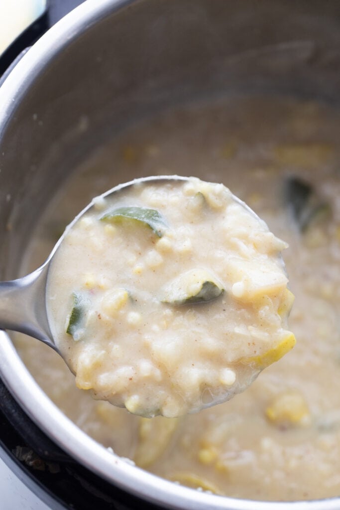 A close up shot of a pot of corn chowder with green and yellow flecks of summer squash and corn kernels visible 