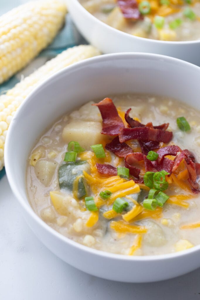 A close up bowl of corn chowder topped with bacon, cheese, and green onions