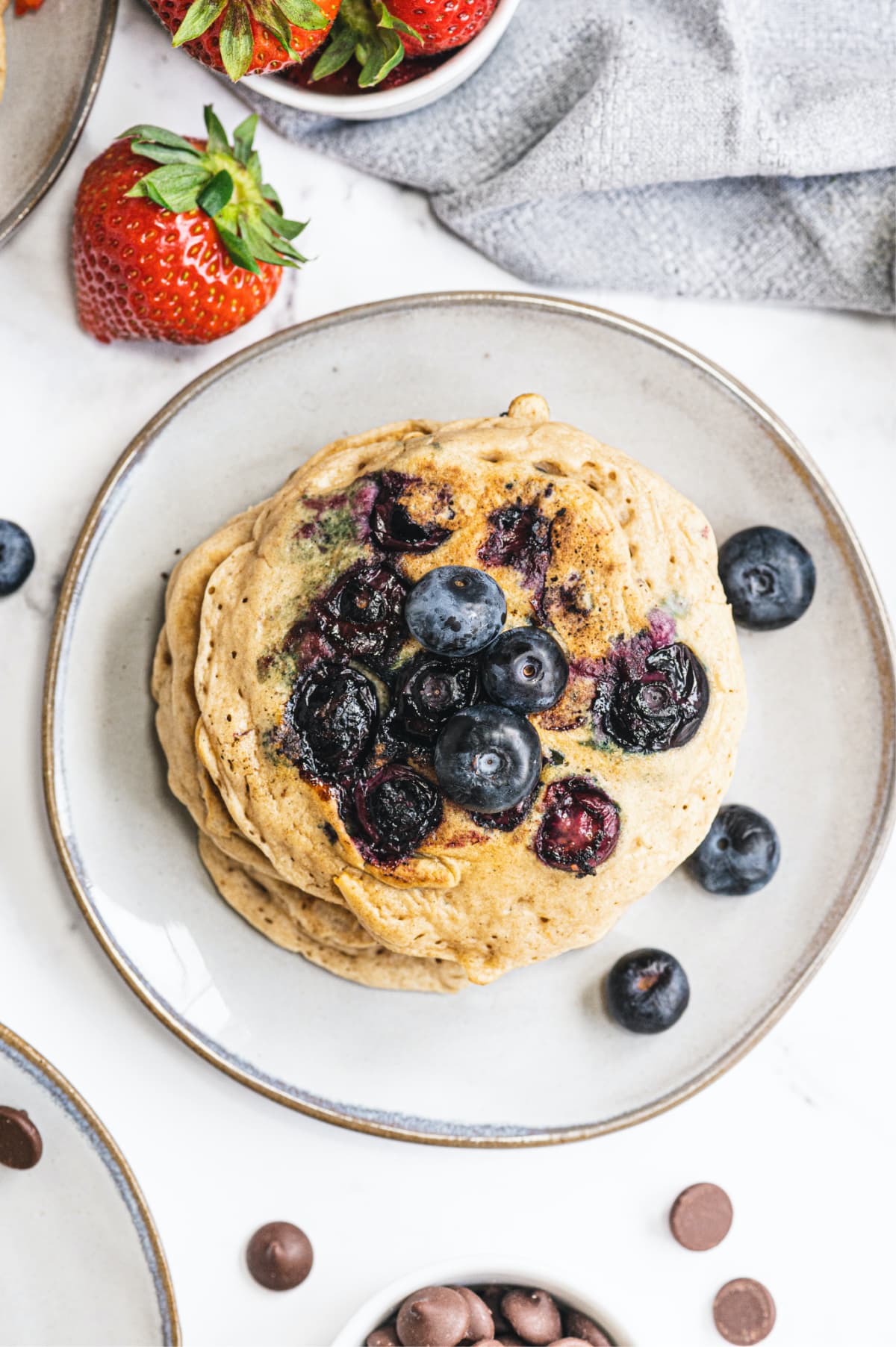 A short stack of Gluten Free pancakes made with blueberries and then topped with additional blueberries on a white plate with a bronze rim.