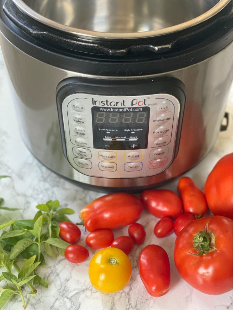 Garden fresh tomatoes of various sizes and homegrown basil in front of an Instant Pot 