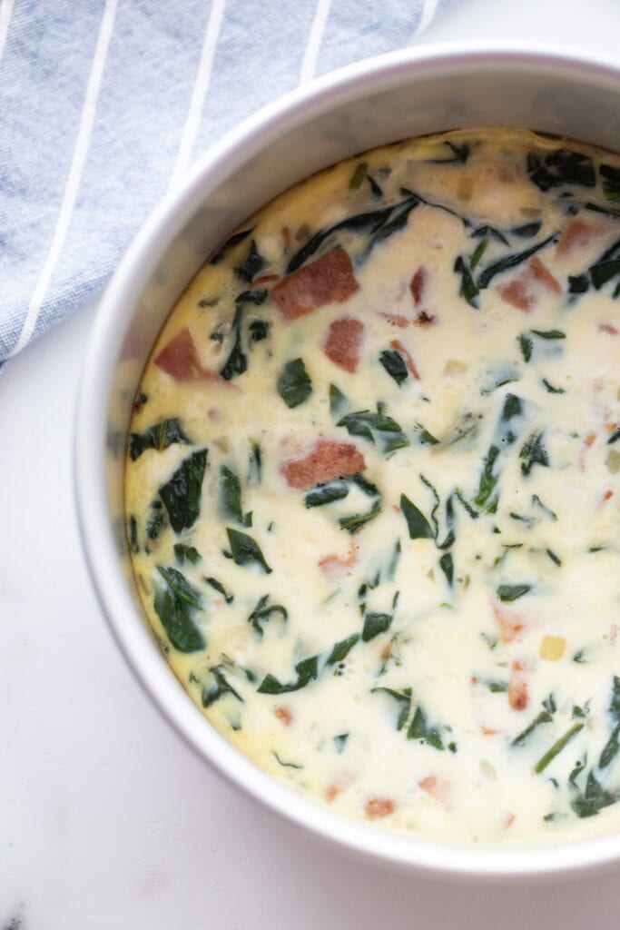 overhead photo: bacon egg and cheese frittata in round white casserole dish