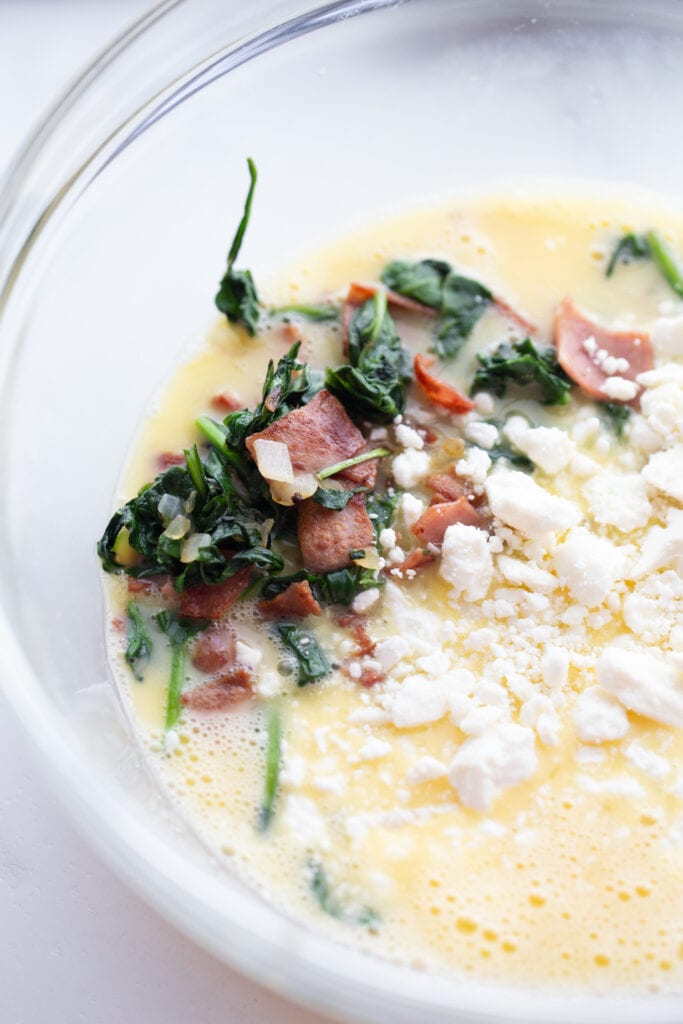 uncooked eggs, spinach, bacon, and cheese in a glass bowl - ingredients for Instant Pot frittata recipe