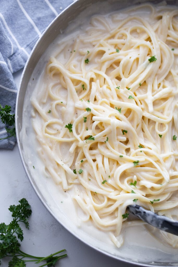 Overhead photo of a pan full of fettuccine alfredo garnished with flecks of parsley. 