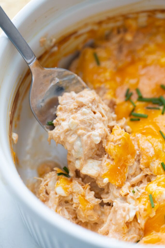 White casserole dish of buffalo chicken dip with a metal spoon serving up a cheesy bite.