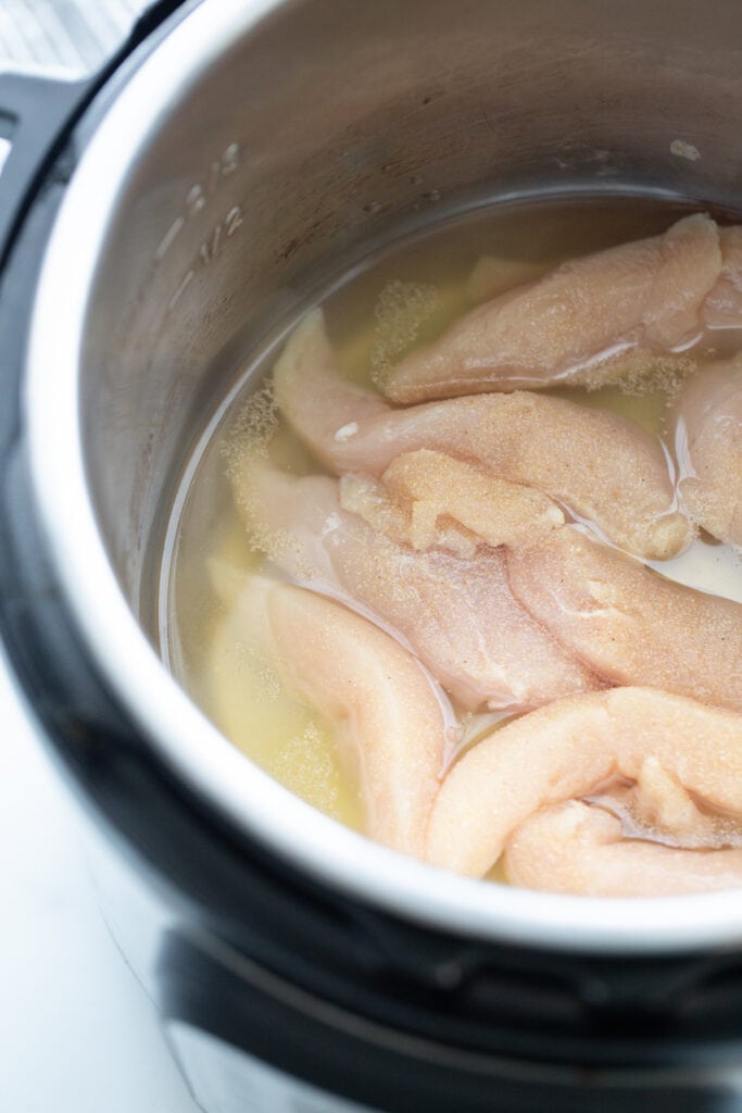 Overhead photo of an Instant Pot with raw chicken and broth, ready to cook and made shredded chicken.