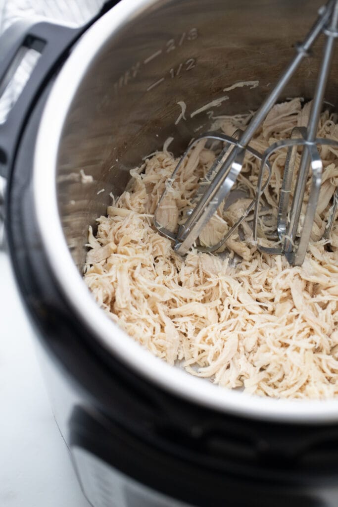 Instant Pot filled with cooked, shredded chicken and mixer blades.
