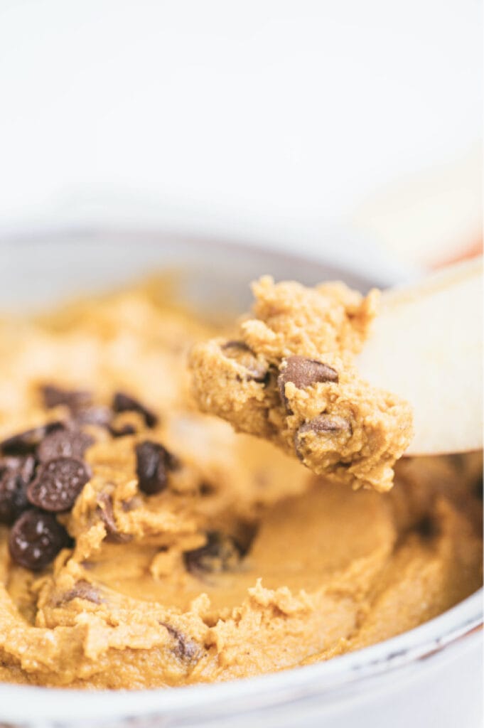 close up of pumpkin cookie dough dip on a spoon over bowl of dip