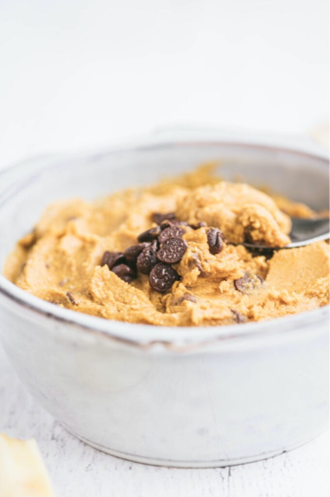 side view: white bowl of pumpkin hummus topped with chocolate chips with a spoon in the dip