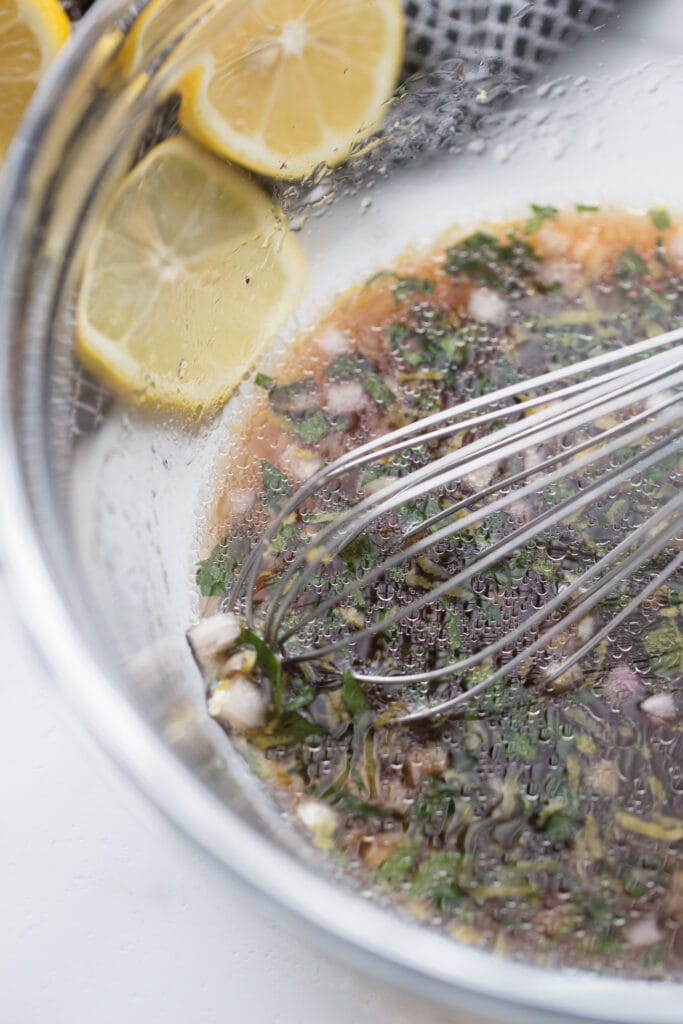 using whisk to combine ingredients for a marinade for shrimp in a clear glass bowl