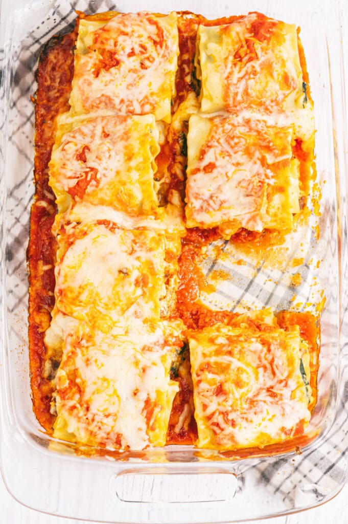 Overhead image: glass baking dish of lasagna rolls topped with sauce and cheese. There is a lasagna roll missing from the dish.