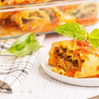 Lasagna roll ups made with spinach, chicken sausage, and cottage cheese being served from a baking dish and plated on a small white plate.