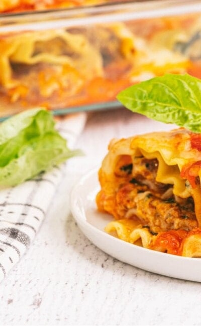 Lasagna roll ups made with spinach, chicken sausage, and cottage cheese being served from a baking dish and plated on a small white plate.