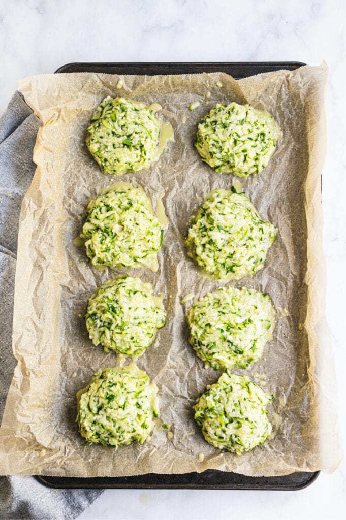 Overhead image: two rows of zucchini fritters on a parchment lined sheet pan, ready for the oven.