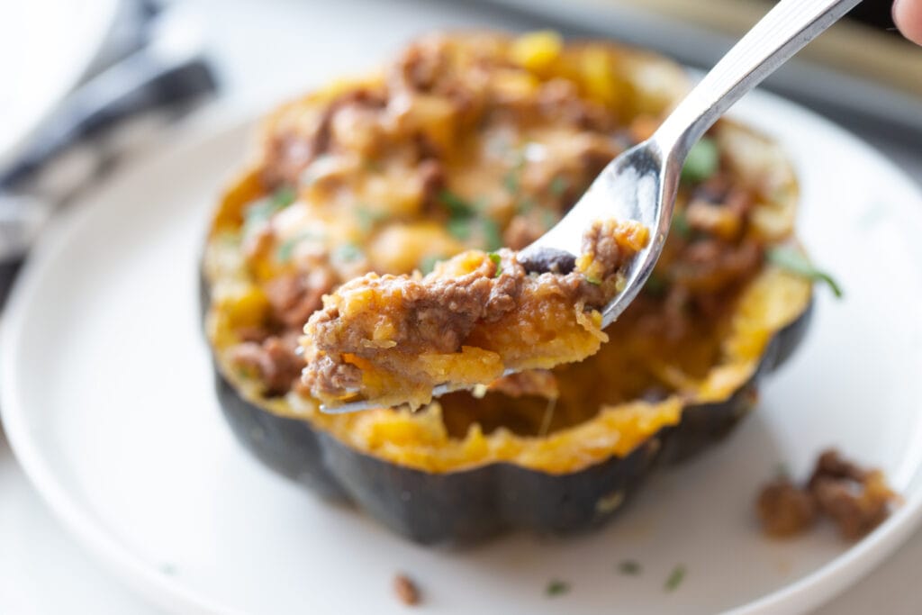 Close up photo of a bite of taco stuffed acorn squash on a fork with the rest of the squash in the background on a plate.
