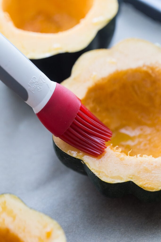 Silicone cooking brush basting half of an acorn squash with olive oil before roasting in the oven.