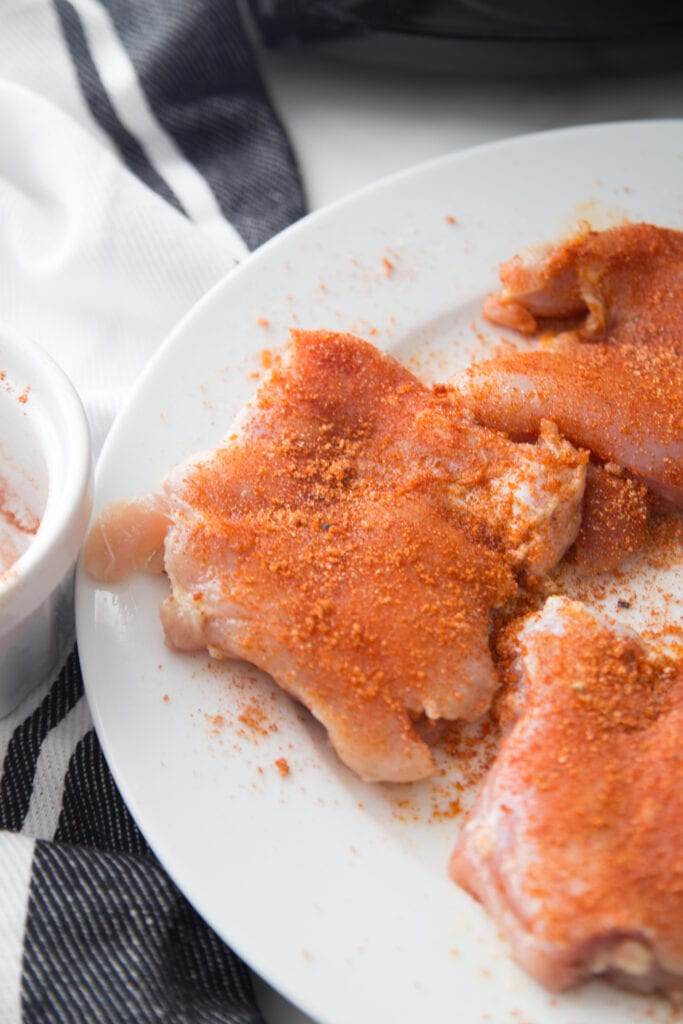 raw chicken thighs with dry rub seasoning on white plate